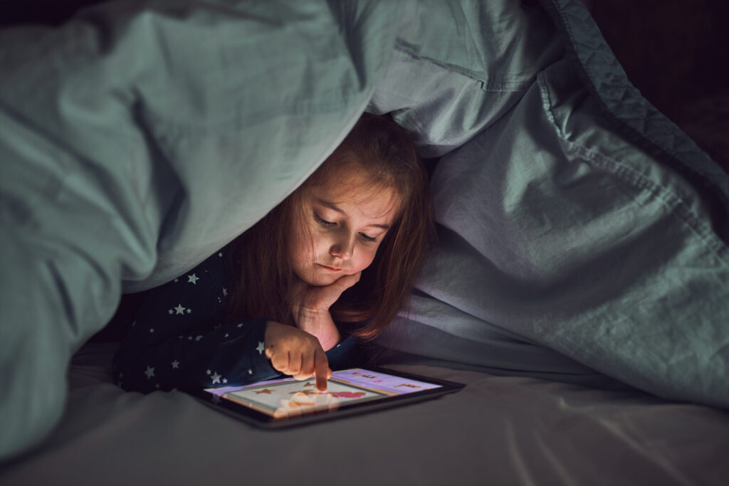 a gen alpha child in bed looking at a tablet